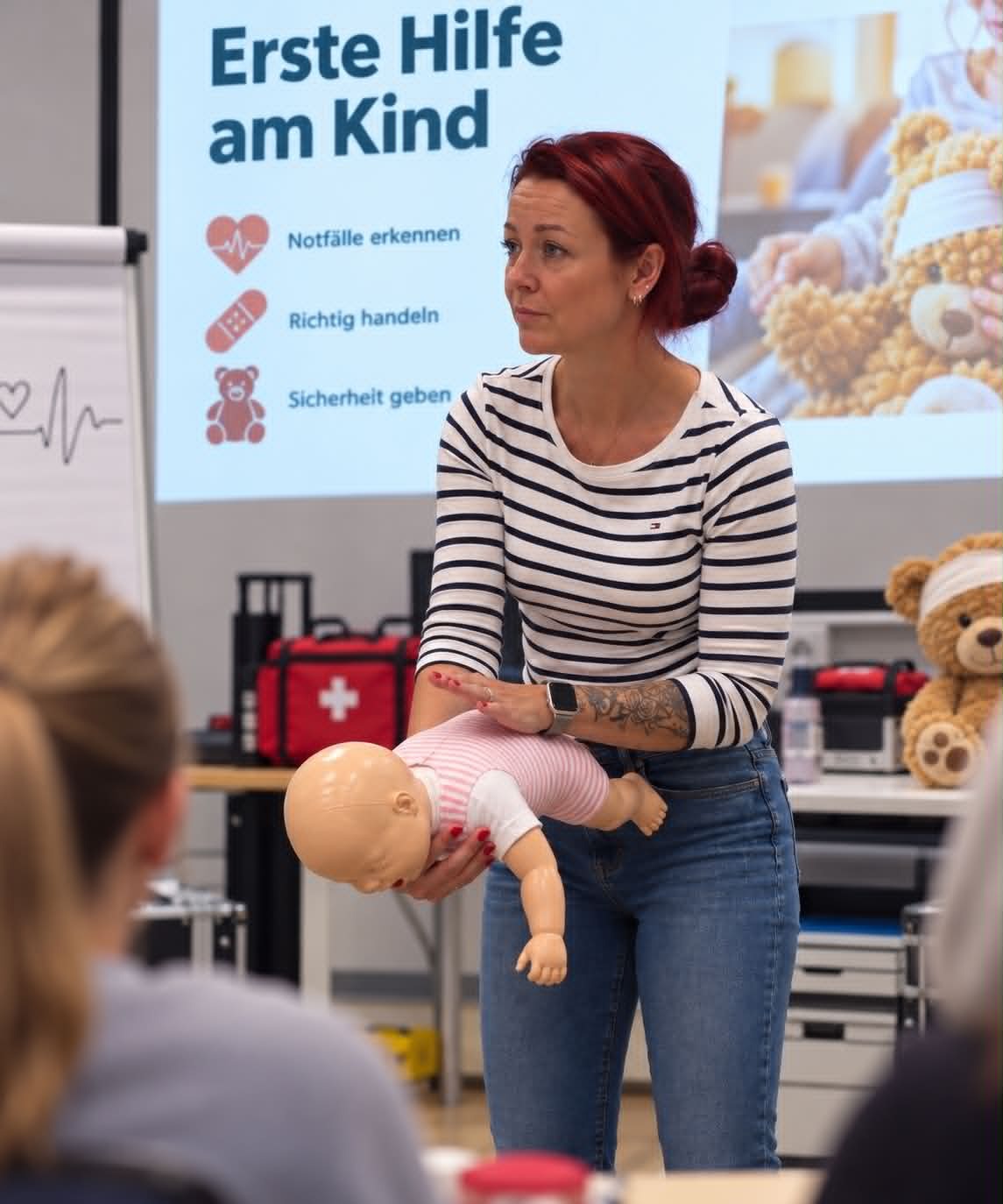 Selin Schuster zeigt an einer Baby-Übungspuppe die Handgriffe bei einem Kindernotfall, im Hintergrund eine Präsentation zum Thema Erste Hilfe am Kind